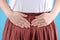 Girl in a white shirt and skirt holding her belly front view, concept of menstruation pain