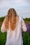 A girl in a white shirt stands with her back to the camera against a lupine field