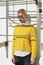 Girl in white shirt sticking out under yellow sweater and blue jeans posing near fire escape