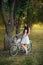 Girl in a white skirt and a vest with a bicycle and a basket full of flowers in the park in the evening