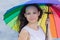 Girl in white sleeveless dress posing with rainbow umbrella