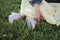 A girl in white sports sneakers and a yellow skirt sits on the grass in the park. Legs and hand closeup