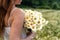 A girl in a white sundress holds a bouquet of white daisies in her hand on a large chamomile field against the background of a