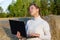 Girl in a white sweater against a background of haystacks and green forest holds a laptop in her hands