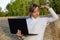 Girl in a white sweater against a background of haystacks and green forest holds a laptop in her hands