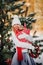 A girl in a white sweater with Christmas gifts in her hands stands in a snow-covered forest.Woman with Christmas gifts outside in