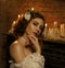 A girl in a white vintage dress with open shoulders stands against the background of an old piano and candles. Gothic