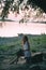 Girl in a white vintage dress with willow and flowers wreath sitting and dreaming near the river on stones