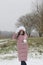 A girl in winter clothes on a walk in the park. Holds a ball of snow in his hand. The ground is covered with the first snow