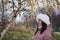 A girl in winter clothes on a walk in the park. Stands near a birch tree with yellowed leaves. The first snow on earth