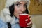 A girl in a winter suit drinks a drink. red mug. brunette babe young caucasian girl wearing a woolly hat holding a red cup,
