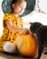 Girl in witch halloween costume sitting on a table playing with pumpkin and her pet cat. Halloween background.