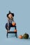 Girl in witch hat and black clothes sits on stepping stool with pumpkin in hand