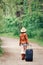 girl woman in leather jacket, blue denim shorts, straw hat, standing walking on country road wild forest with travel bag