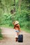 Girl woman in leather jacket, blue denim shorts, straw hat, standing walking on country road wild forest with travel bag