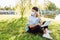 Girl working at the computer sitting on the grass near the lake in a protective medical mask on her face and have a phone talk.