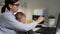 Girl works at computer. Attractive woman sits at desk typing on laptop keyboard and holds in her arms small child who