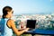 The girl works on a computer in a cafe on the roof. Female writing on a laptop in a rooftop cafe, sitting at a wooden