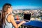 The girl works on a computer in a cafe on the roof. Female writing on a laptop in a rooftop cafe, sitting at a wooden