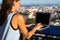 The girl works on a computer in a cafe on the roof. Female writing on a laptop in a rooftop cafe, sitting at a wooden