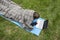 Girl wrapped in a gray woolen plaid is working with a laptop while lying on a sports mat in a meadow by the river