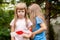 Girl wrapping her sister in red white security tape. Happy school age children, cheerful girls, siblings or friends playing