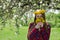 Girl in a wreath of dandelions stands under blossoming apple tree and sniffs a bouquet