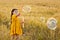 A girl in a yellow dress is playing in a wheat field and blowing soap bubbles. Nature in the village