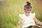 Girl in a yellow dress sits in the grass on a blanket in a field and reads a paper book. International Children`s Day. Summer tim