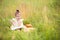 Girl in a yellow dress sits in the grass on a blanket in a field and reads a paper book. International Children`s Day. Summer tim