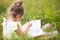 Girl in a yellow dress sits in the grass on a blanket in a field and reads a paper book. International Children`s Day. Summer tim