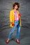 Girl in a yellow jacket and blue jeans with an afro hairstyle. Fashion of the eighties, disco era.