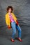 Girl in a yellow jacket and blue jeans with an afro hairstyle. Fashion of the eighties, disco era.