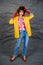 Girl in a yellow jacket and blue jeans with an afro hairstyle. Fashion of the eighties, disco era.