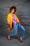 Girl in a yellow jacket and blue jeans with an afro hairstyle. Fashion of the eighties, disco era.