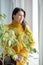 A girl in a yellow sweater is sitting in fresh green leaves looking out the window. Spring freshness and beauty
