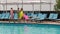 Girlfriends in bathing suit go along wooden pier on background swimming-pool with blue water, young women