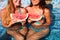 Girlfriends holds half a red watermelon over a blue pool, relax