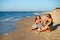 Girlfriends laughing and eating fresh watermelon at seaside in the morning. Two happy women friends sitting on towel and