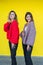 girlfriends posing together in modern knitted sweaters isolated on yellow wall studio portrait