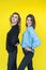 girlfriends posing together in modern knitted sweaters isolated on yellow wall studio portrait