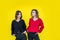 girlfriends posing together in modern knitted sweaters isolated on yellow wall studio portrait