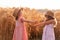 Girlfriends tickle each other`s nose with spikelets of rye. Little girls in straw hat are having fun