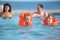 Girls bathing in life jackets with parents in pool