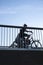 Girls cycling on bicycle bridge. Silhouettes seen from low angle through bars in metal railings.