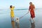 Girls With Dog On Beach. Barefoot Women In Maxi Boho Dresses Enjoying Summer Vacation With Pet