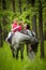 Girls enjoying horseback riding in the woods with mother, young pretty girls with blond curly hair on a horse, freedom