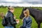 Girls feed a black horse on a green lawn in the fall.