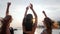 Girls have fun on embankment, best girlfriends dancing in the sunset on beach, three female raises arms up on seaside