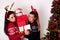 Girls holding many heavy gift boxes next to Christmas tree in sweater and reindeer horns